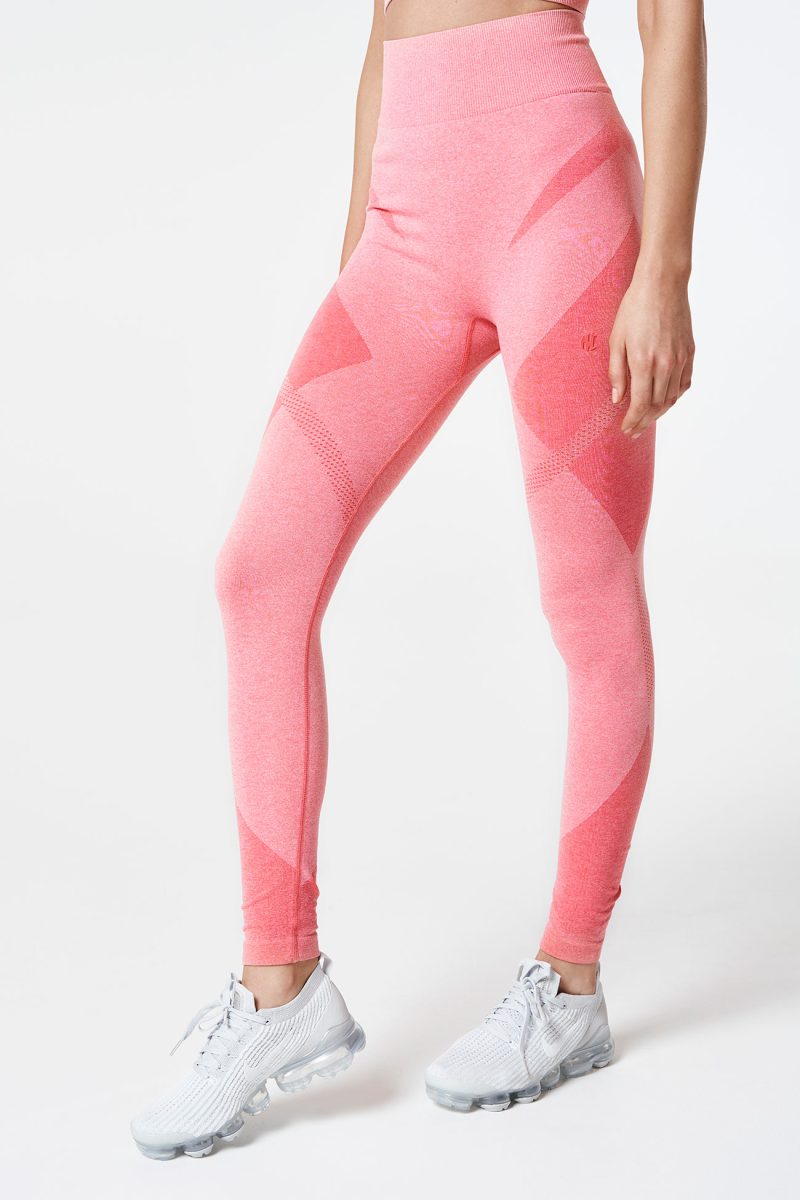 Close-up of a brunette woman’s legs standing, dressed in coral pink Bold Seamless Performance Leggings, emphasizing the sleek fit and bold color of the leggings.