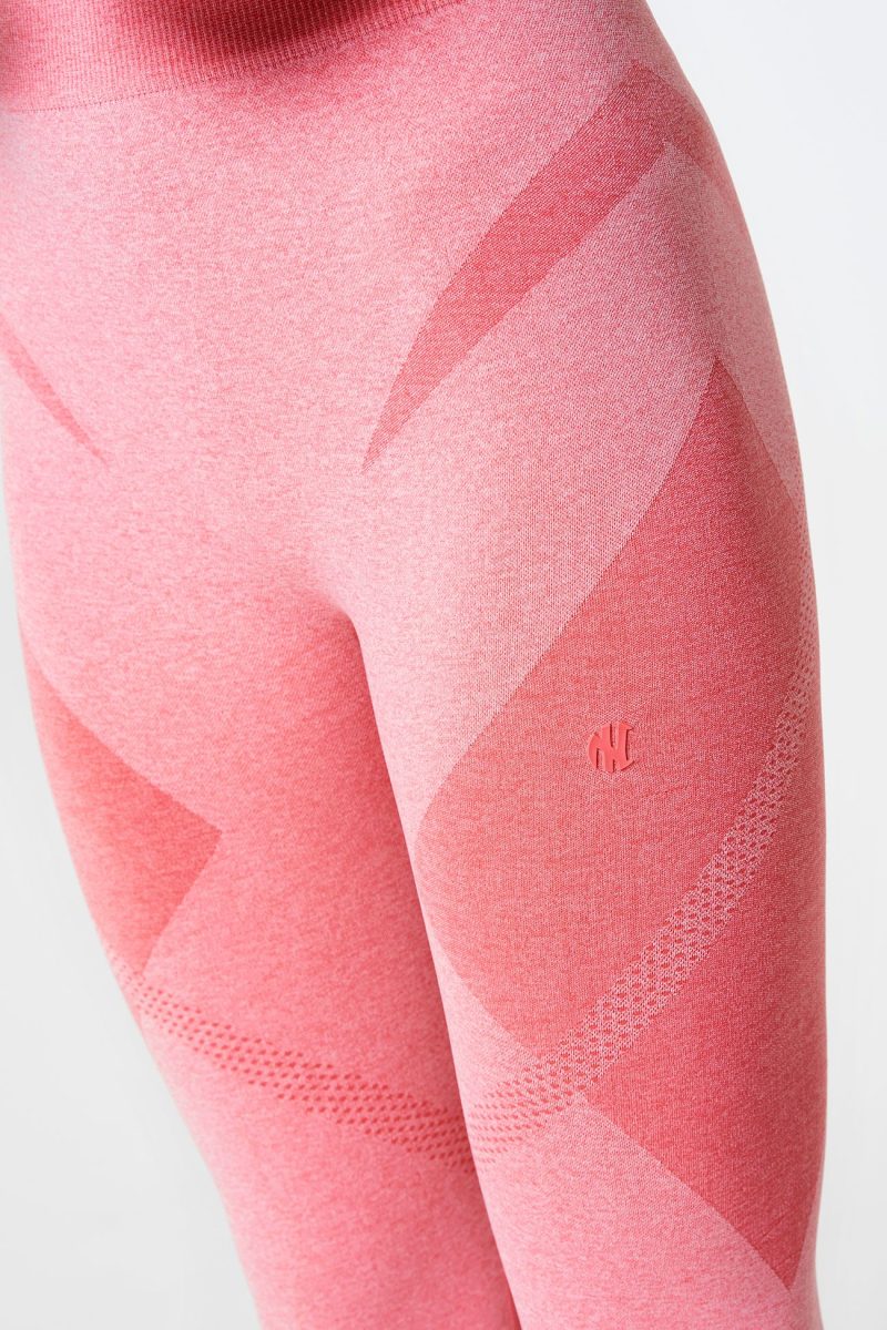 Close-up of the front of a brunette woman’s legs, wearing coral pink Bold Seamless Performance Leggings, with the NexLevel logo visible, highlighting the beautiful design and perfect fit.