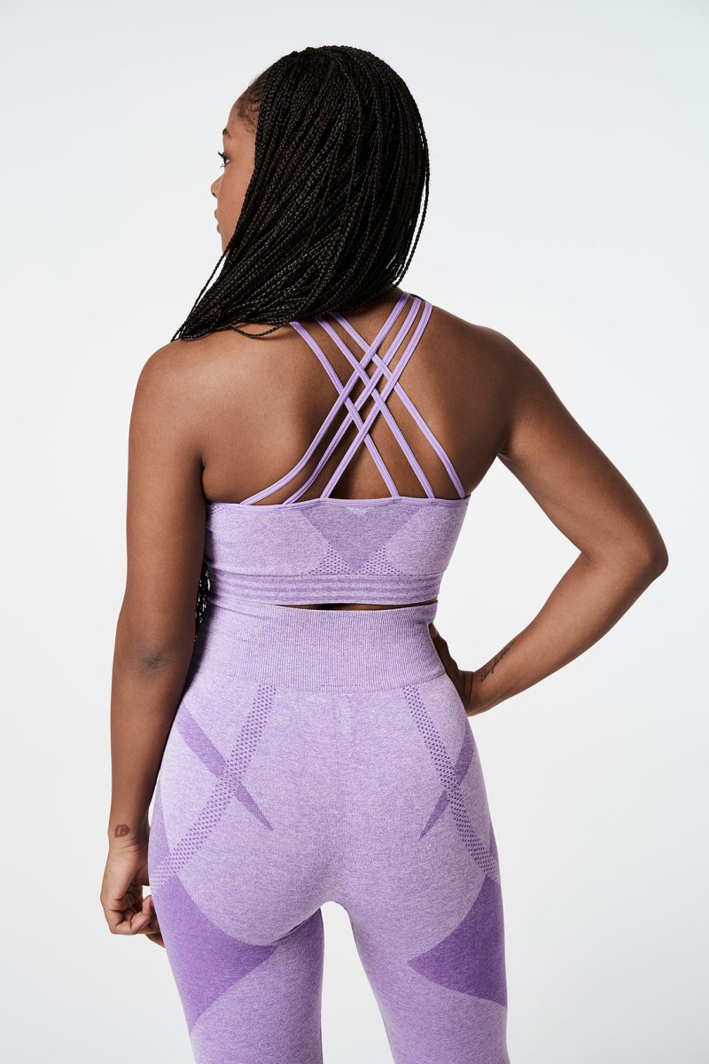 Black woman from the back, wearing a Violet Bold Seamless Performance Strappy Back Sports Bra and matching leggings, with one hand on her hip, showcasing a confident and stylish pose.