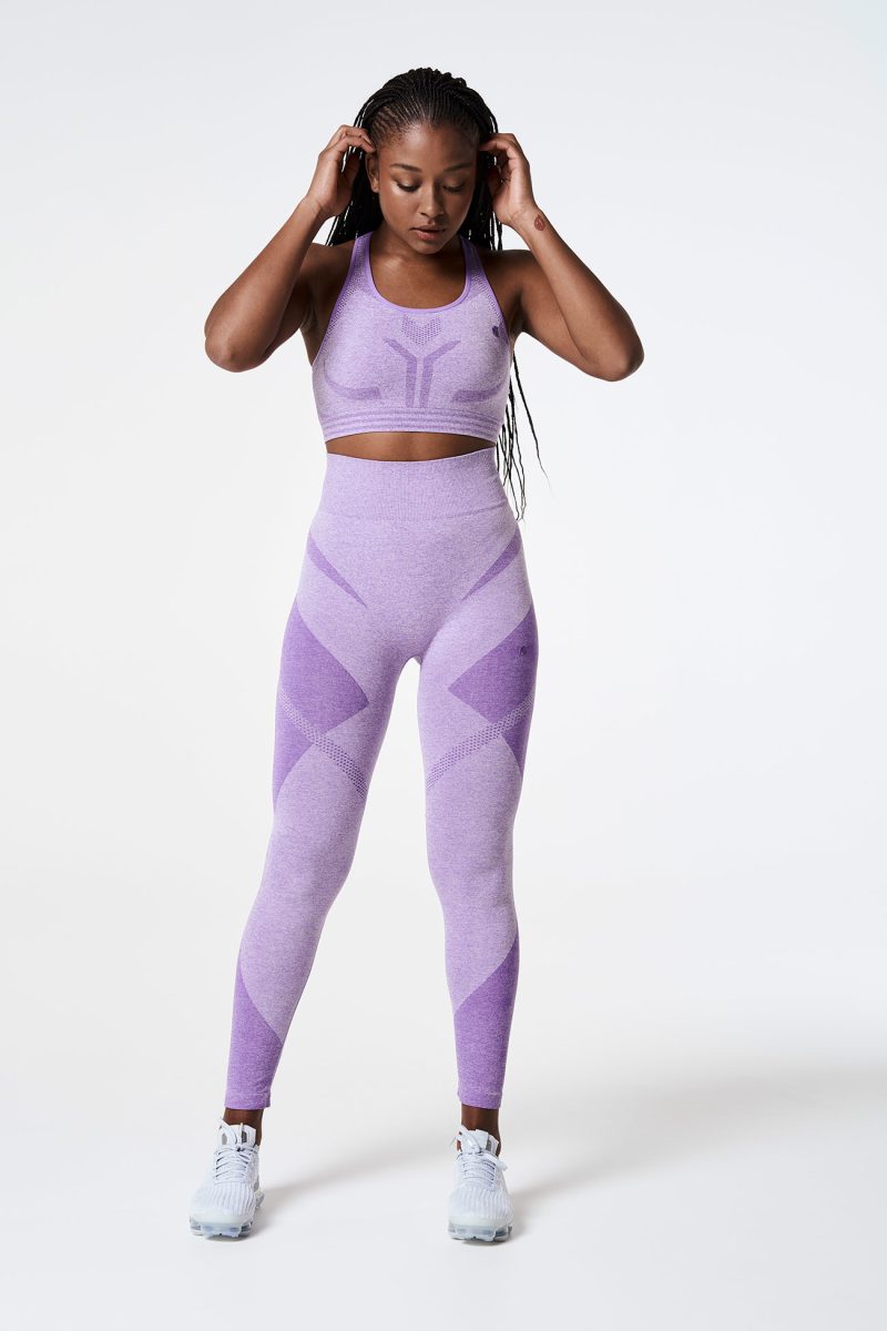 Full-body shot of a Black woman looking down, wearing a Violet Bold Seamless Performance Strappy Back Sports Bra and matching leggings, highlighting the coordinated and sleek athletic look.