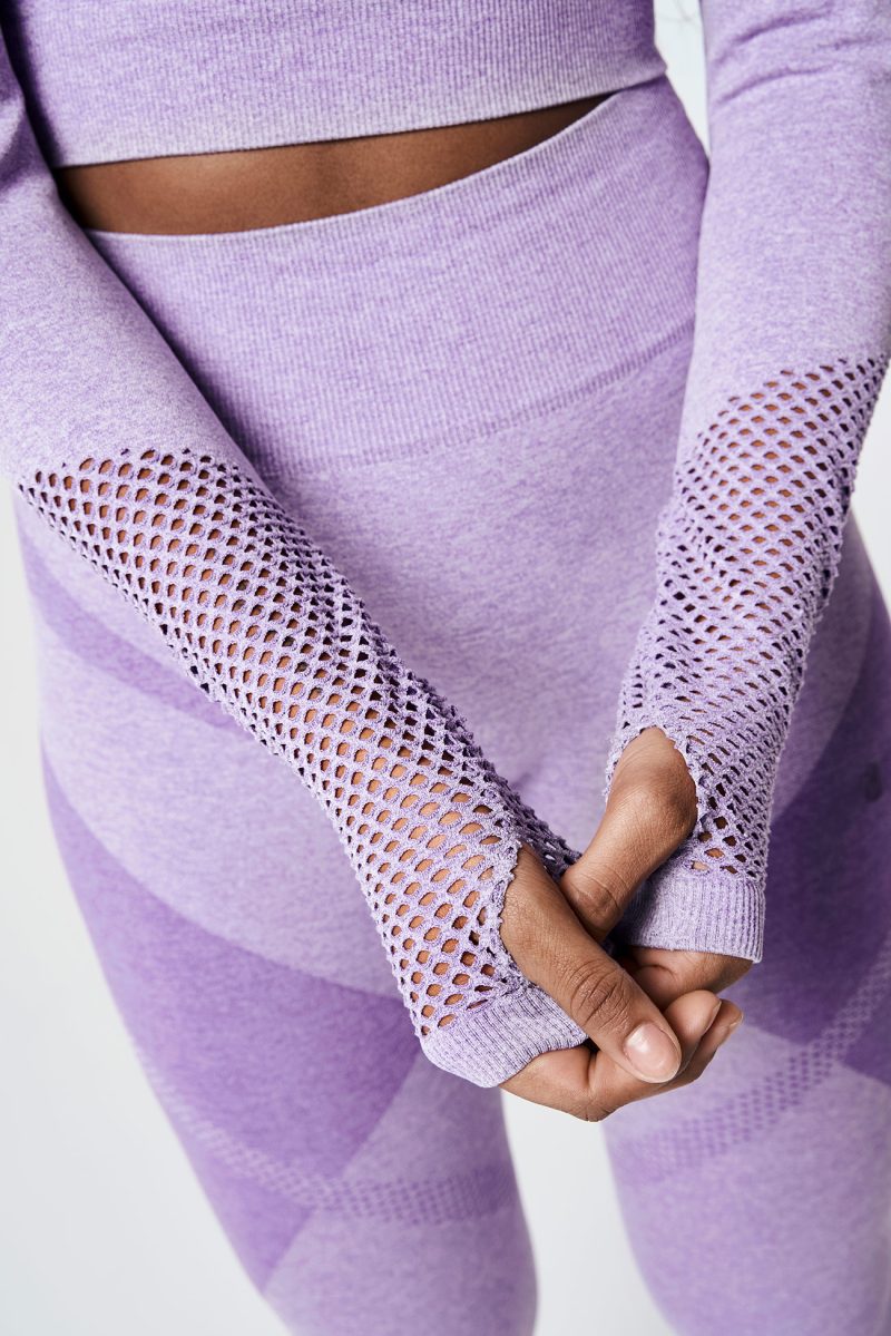 Close-up of a Black woman's arms, wearing a violet pink bold seamless performance long-sleeve crop top with mesh details, highlighting the sleek design and athletic style.