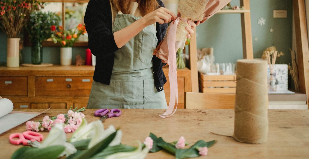 Girl in flower shop doing a beautiful coral pink bouquet of flowers 