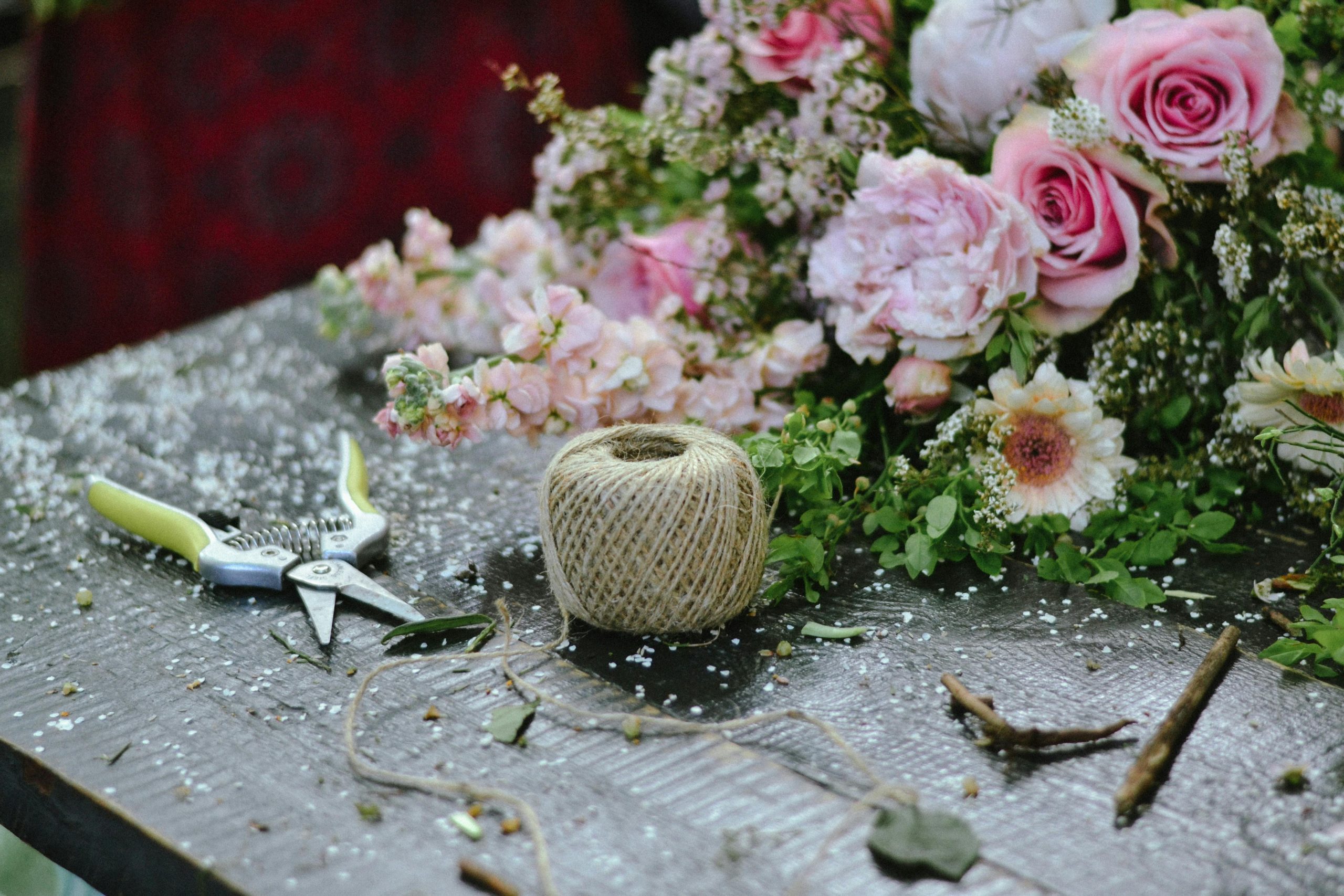 Coral pink flowers arranged on a rustic bench with a pair of scissors and twine, ready to be crafted into a beautiful bouquet